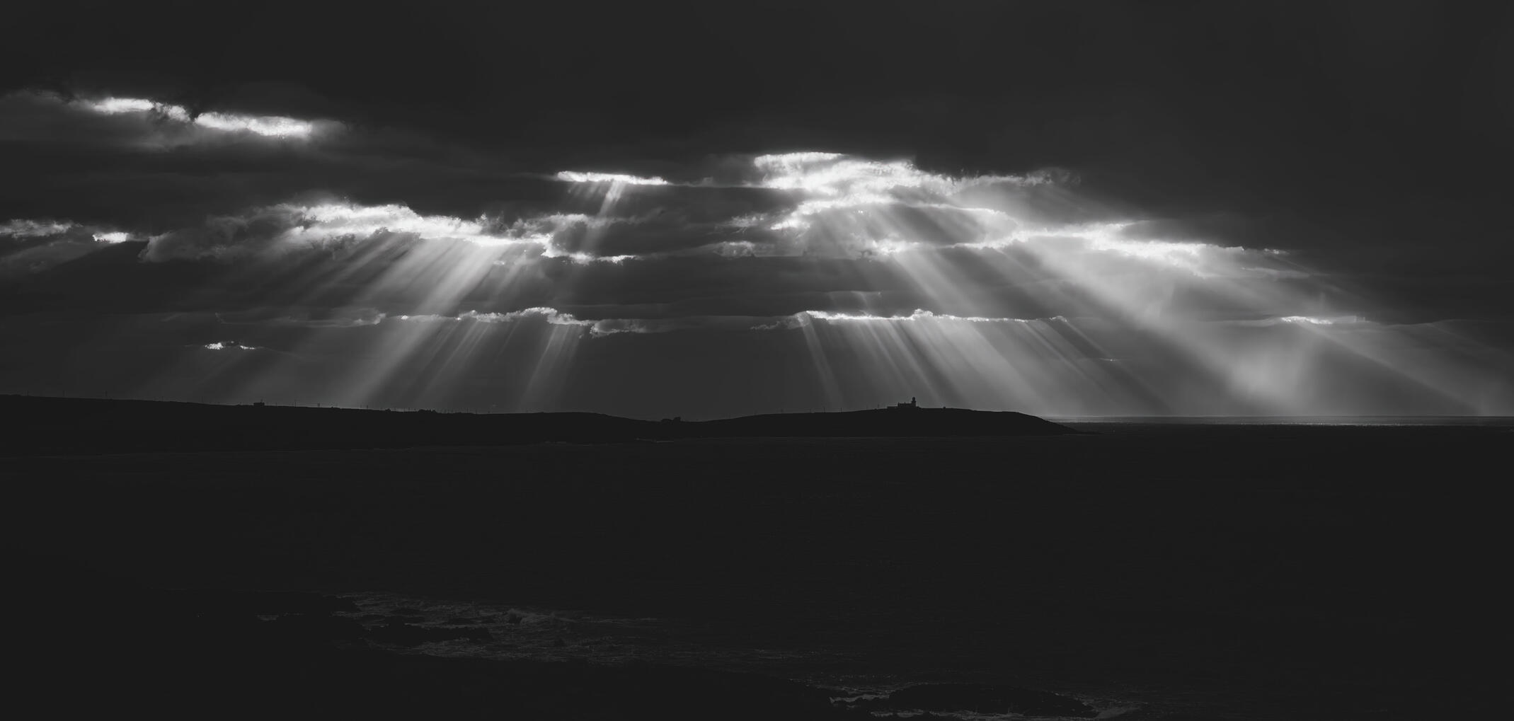 Dramatic black and white photograph of sunlight streaming through storm clouds over the West Cork coast.